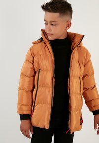 Orange puffer jacket with a shiny finish, featuring a hood, front zipper, and elastic cuffs. Black sweater beneath, with a smooth texture.
