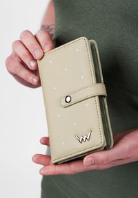 Light green wallet with white polka dots, featuring a snap closure and gold logo accent. Smooth texture and rectangular shape.