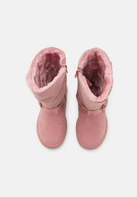 Růžové semišové boty s umělým kožíškem podél vnitřku, zapínáním na zip a dekorativním páskem s knoflíkovým detailem. Hladká textura a výška po střed lýtka.