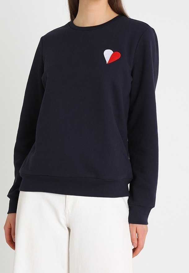 Sweat-shirt bleu marine à manches longues, col rond, avec une petite broderie de cœur rouge et blanc sur la poitrine. Tissu doux et texturé.