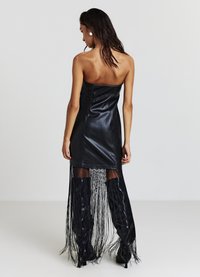 Robe bustier en simili cuir noir avec une fente haute sur la cuisse, des détails à franges longues, et des bottes à talons hauts. Texture lisse.