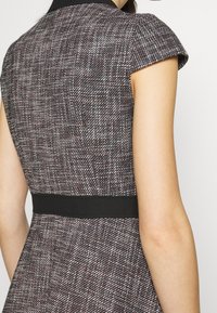 Sukienka dopasowana, wykonana z fakturowanej tkaniny tweed w kolorach czarnym, białym i burgundowym. Posiada krótkie rękawy i czarną talię.