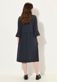 Czarna sukienka w granatowym kolorze z rozszerzanymi rękawami, z marszczonym szwem w talii i gładką fakturą. Prosta i zwiewna sylwetka.