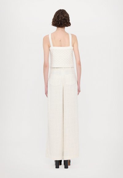 White textured cropped top with wide straps, paired with high-waisted, wide-leg off-white pants with pockets. Smooth, woven fabric.