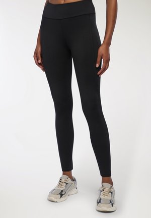 Leggings neri a vita alta con una texture liscia e un design aderente, abbinati a sneakers beige e grige con una suola spessa.