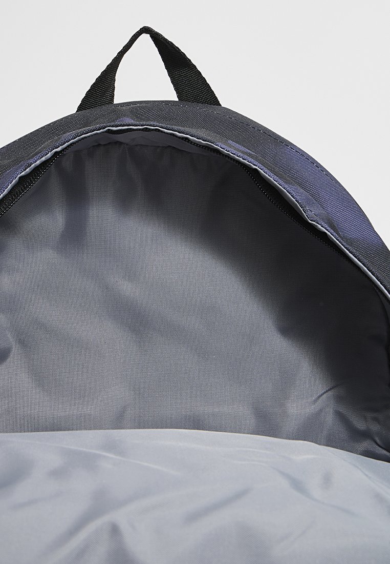 Innenansicht eines Rucksacks mit glattem, grauem Stofffutter und einer strukturierten schwarzen Außenkante. Enthält eine obere Aufhängeschlaufe für leichteren Transport.