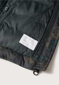 Zwarte gewatteerde stof met een ingeweven wit label waarop lege velden voor "Naam" en "Telefoon" naast de ritsrand.