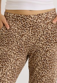 Pantalon à imprimé léopard de couleur beige clair, avec une texture de tissu lisse, deux poches latérales et une taille élastique.