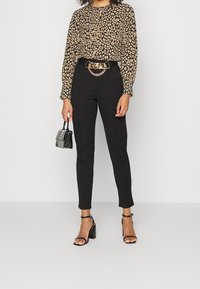 Blouse à impression léopard avec manches longues, pantalon noir taille haute, ceinture en chaîne dorée et escarpins noirs à lanières, accompagnés d'un petit sac à main.