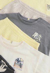 Quatre tenues décontractées pliées avec des hauts imprimés aux motifs sur le thème de la plage et des shorts à taille élastique texturés assortis dans des couleurs pastel douces.