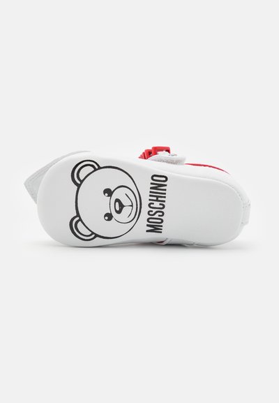 White shoe sole with a black bear graphic and "MOSCHINO" text, accented with red trim and a textured surface.