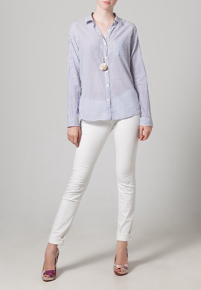 Blauw en wit gestreept overhemd met knopen, witte slim-fit broek en meerkleurige hoge hakken; casual outfit met opgerolde mouwen.