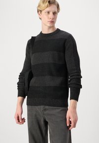 Maglione a maglia con un motivo a righe in nero e grigio scuro, con polsini e orlo a coste, tessuto testurizzato, indossato con una borsa a tracolla nera.