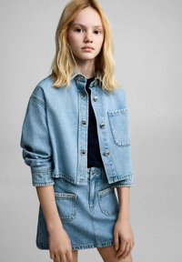 Denim jakna i suknja u svijetloplavoj boji; jakna ima dugmadi na gumbe, jednu džep na prsima i spuštene ramena; suknja ima dva prednja džepa.