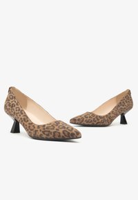 Tacchi alti in stampa leopardata, realizzati in tessuto morbido, con punta affusolata e tacco basso a blocco. I colori dominanti sono marrone e nero.