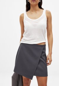 Un débardeur blanc sans manches et transparent associé à une jupe enveloppante gris foncé avec une texture lisse et des bords nets.