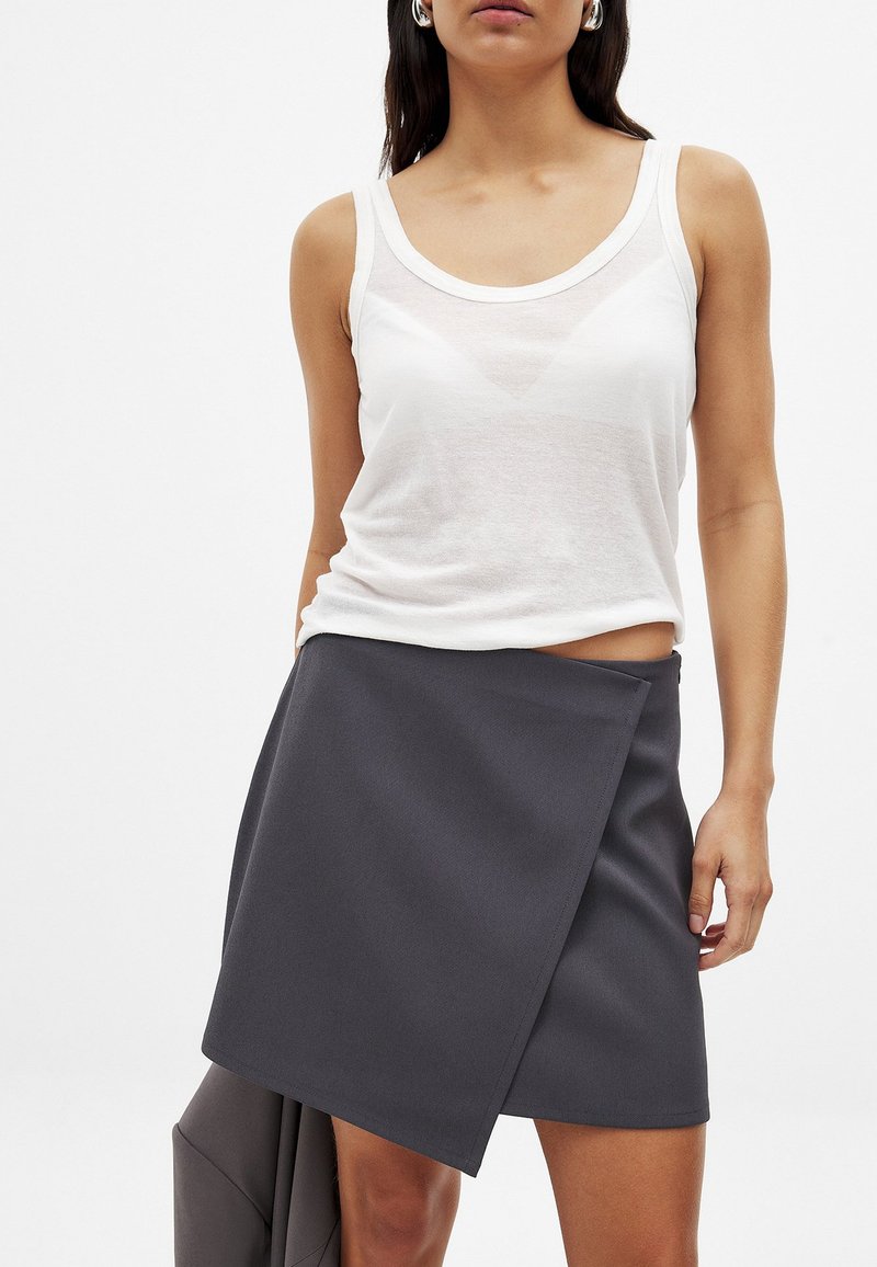 Un débardeur blanc sans manches et transparent associé à une jupe enveloppante gris foncé avec une texture lisse et des bords nets.