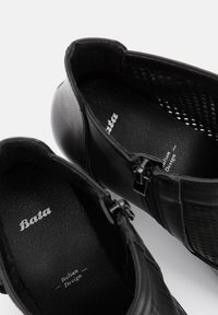 Black leather ankle boots with a textured finish, featuring zippers on both sides and “Bata Italian Design” embossed on the insoles.