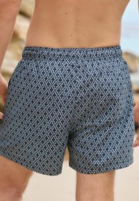 Plave kupaćice s uzorkom, izrađene od materijala koji brzo suši, s geometrijskim dizajnom, elastičnom waistbandom i dužinom iznad koljena.