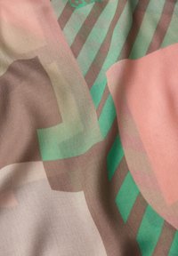 Tissu à motifs abstraits composé de couches de textile doux et translucide dans des nuances de vert, rose et marron avec des dessins géométriques.