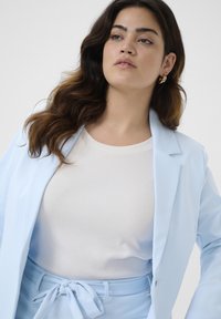 Světle modrý blazer s jednobuttonovým zapínáním přes bílé žebrované tričko. Blazer má klopové límce a odpovídající pásek v pase.