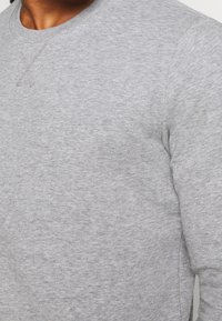 Šedá mikina s kulatým výstřihem, měkkou texturou a jemnými švy. Vyrobena z bavlněné směsi pro pohodlí.