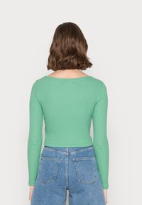 Langärmliges, geripptes grünes Oberteil mit Rundhalsausschnitt, kombiniert mit hochgeschnittenen blauen Denim-Shorts mit zwei Rückentaschen.