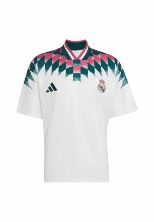 Maillot de football blanc du Real Madrid avec motif géométrique rose et vert sur les épaules, logo Adidas à gauche, écusson du club sur la poitrine droite.