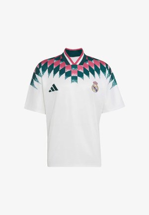 Maillot de football blanc du Real Madrid avec motif géométrique rose et vert sur les épaules, logo Adidas à gauche, écusson du club sur la poitrine droite.