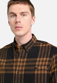 Camicia a quadri nera e marrone con colletto button-down. Presenta bottoni scuri e due tasche sul petto, realizzata in un tessuto testurizzato.