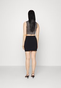 Top court noir avec un motif de texte, associé à une jupe noire ajustée. Le mannequin porte des sandales à talons noires et est de dos.