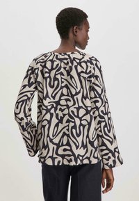 Maglia a maniche lunghe, ampia, di colore beige con motivi astratti neri. Collo rotondo, tessuto texture e silhouette rilassata.