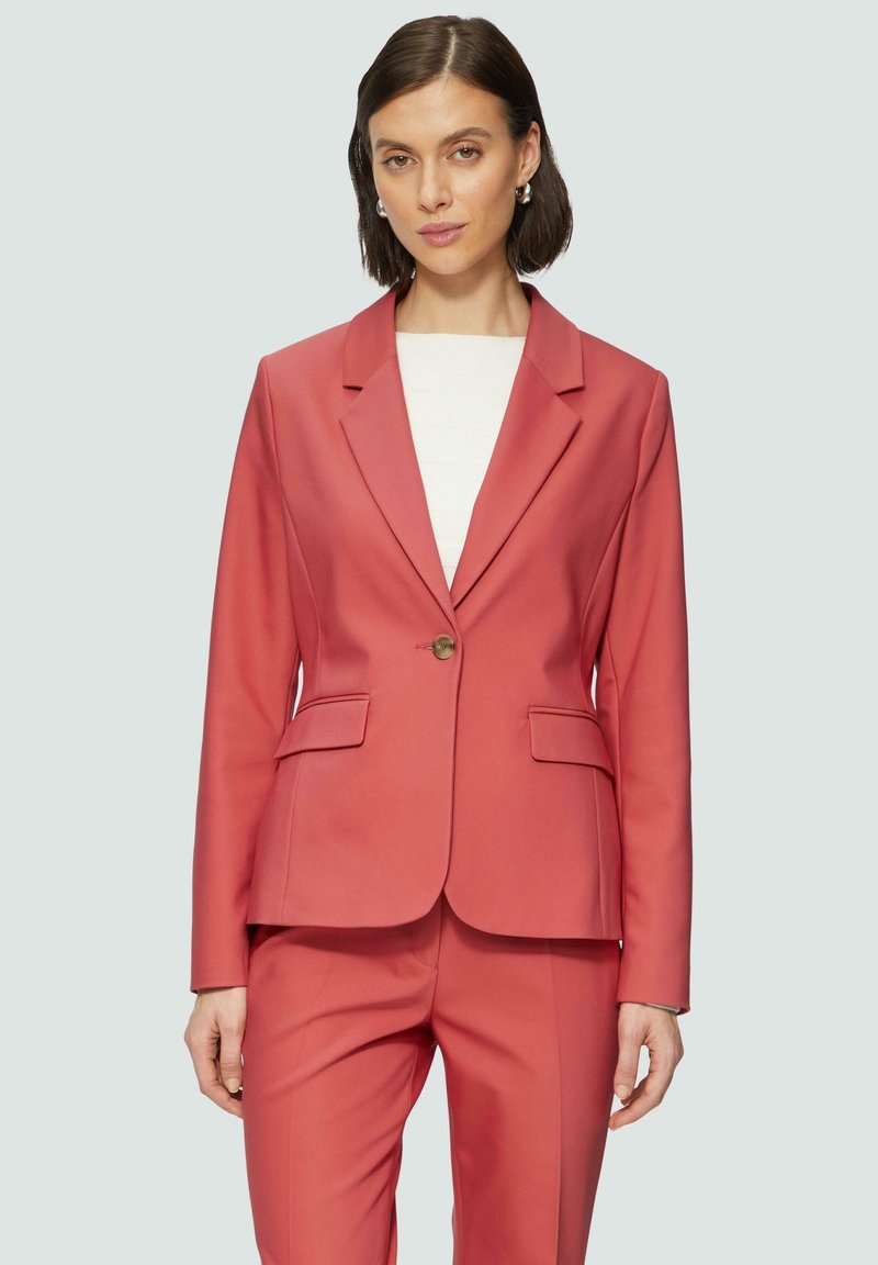 Rosa Blazer und passende Hose aus einem glatten Stoff. Der Blazer verfügt über Reverskragen, einen einzigen Knopf und Fronttaschen.