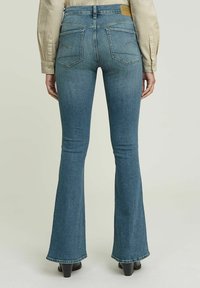 Utsvängda blå denimjeans med medelhög midja, kraftiga sömmar, två bakfickor och en läderpatch vid bakre midjan.