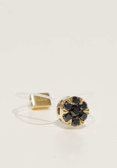 Gold-tone ring with a floral design featuring black gemstone accents. Transparent band with a small square metal detail.