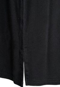 Nahaufnahme eines schwarzen Stoffes mit einer vertikalen Naht und einem kleinen Schlitz am unteren Saum des Kleidungsstücks.