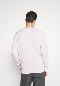 Ljusrosa sweatshirt med långa ärmar, rund hals, ribbade mudd och fåll. Har en liten triangel detalj vid halsringningen.