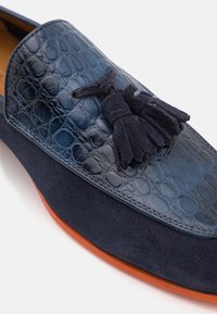 Mocasines de color azul marino con upper de cuero texturizado de cocodrilo, detalles en ante y adorno de flecos; suela de goma naranja.
