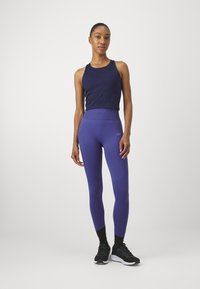 Marineblå tanktop og lilla leggings med ribbet liv, med en glatt tekstur og subtil logo detalj, kombinert med svarte treningssko.