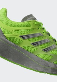 Svijetlozelena sportska cipela s mrežastim stranama, prozračnim materijalom, sivim đonom i tri sive pruge uzduž bočne strane.