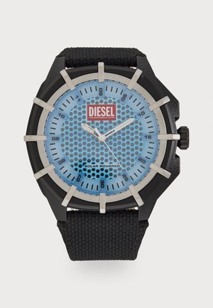 Montre noire solaire avec un cadran perforé bleu, des accents argentés, des marqueurs d'heure audacieux et un bracelet noir texturé. Logo de la marque affiché.