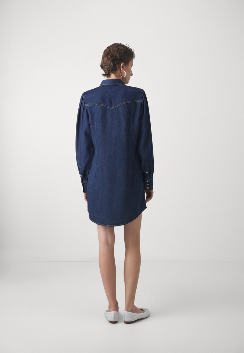 Robe en jean bleu foncé, dotée d'un col, de longues manches bouffantes avec des accents de boutons, et d'un ourlet arrondi. Texture lisse.