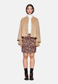 Beige wool blend cropped jacket with silver buttons, white turtleneck, burgundy floral print skirt, black socks, and shiny burgundy footwear.