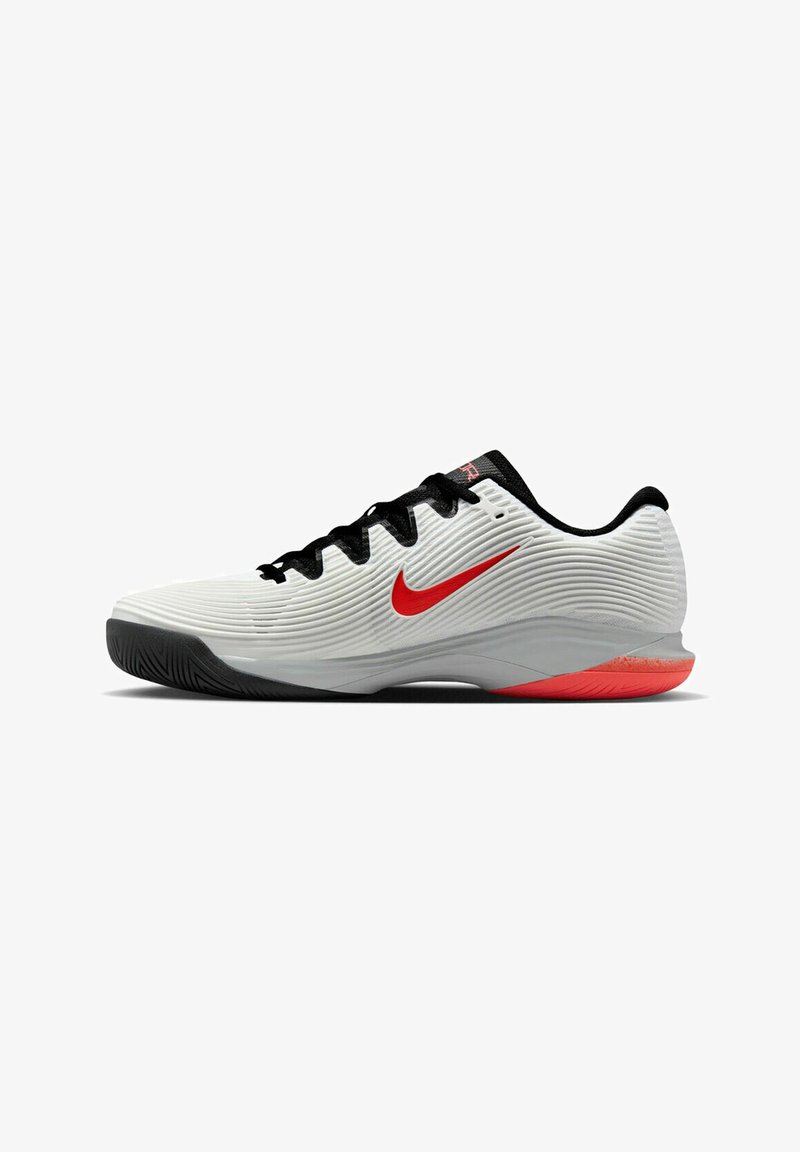 Zapatillas deportivas blancas con parte superior texturizada, acentos en negro y un logo de Nike en rojo. La suela exterior presenta un patrón antideslizante para mayor tracción.