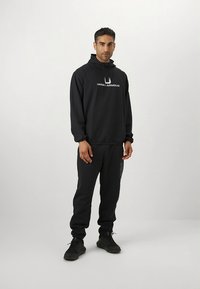 Completo nero con felpa con cappuccio e pantaloni della tuta, con logo Under Armour. Il tessuto è liscio, con vestibilità comoda e polsini elastici.