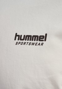 Primer plano de tela blanca con el logo de texto "hummel SPORTSWEAR" impreso en negro en la superficie.