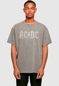 Grå oversized t-shirt i blød bomuld med et falmet AC/DC-logo i hvid. Korte ærmer og en rund halsudskæring. Båret med sorte bukser.