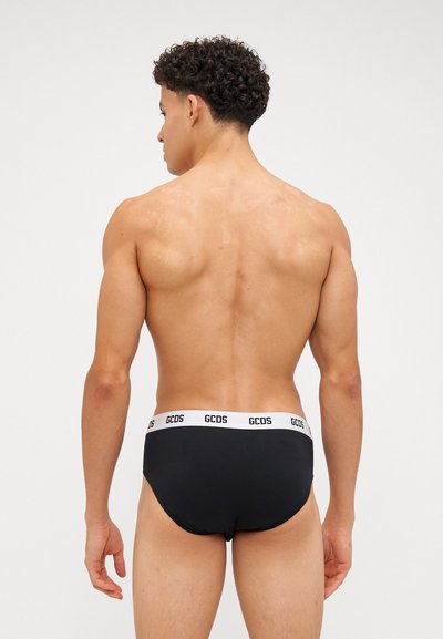 Slip da nuoto nero con una cintura elastica bianca con il branding "GCDS". Tessuto liscio e design aderente. Visto da dietro.