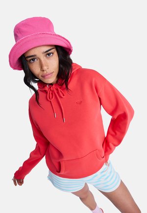 Jasna koralowa bluza z kapturem ze sznurkiem i przednią kieszenią, w połączeniu z jasnoniebieskimi spodenki w paski oraz różowym kapeluszem typu bucket.