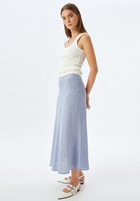 Helles blaues, knielanges Kleid mit diagonalen weißen Streifen, schwingender Form, kombiniert mit einem weißen, gerippten Tanktop und weißen spitzen Ballerinas.